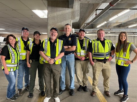 A group of eight men and women standing in a parking garage wearing yellow vests