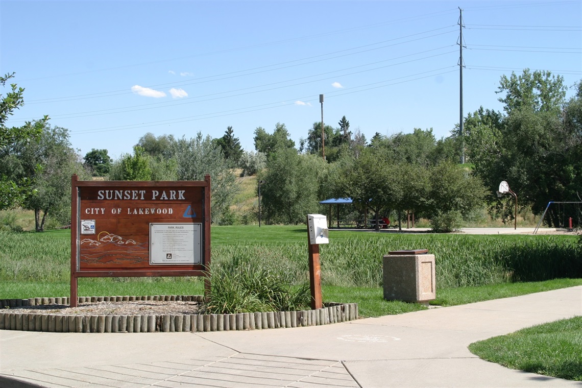 Sunset Park sign with picnic shelter and basketball court in background