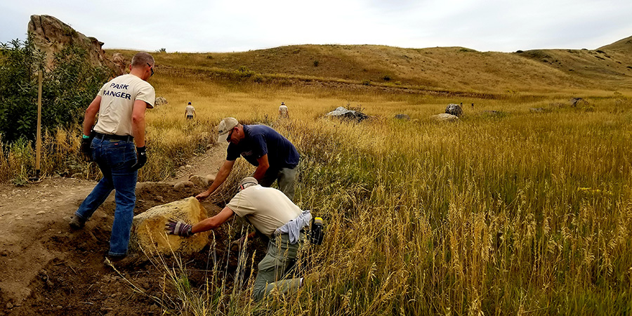 The trail crew moves a rock from a trail area.