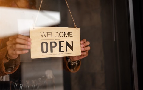 someone holding a welcome open sign in the window