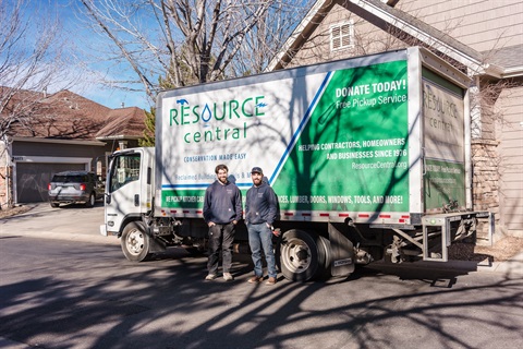 Two men standing next to a white and green truck parked in front of a house.