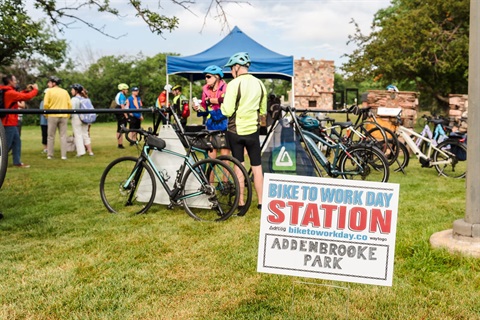 Bicyclists standing next to bikes at a bike to work day station.