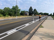 a street with a sidewalk next to it with trees lining it. A biker is biking in the bike lane.