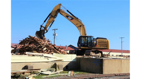 back hoe lifting wood debris from a pile